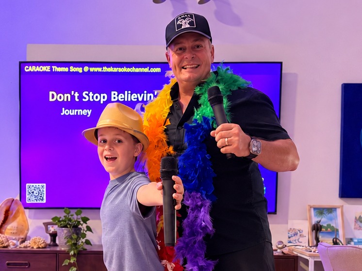 Paul and Jasper Guerin singing with microphones in front of a colourful CARAOKE karaoke screen